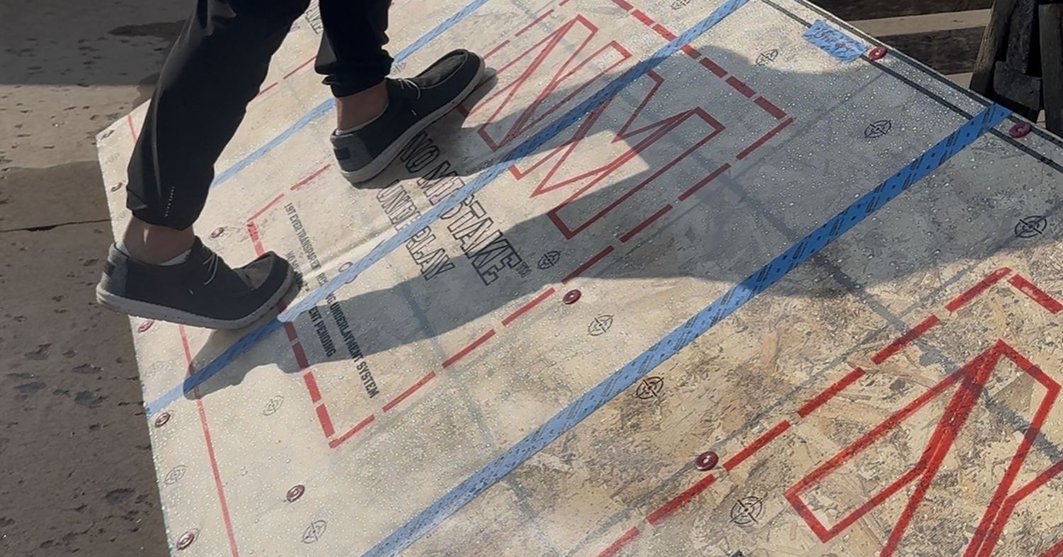 Close view of work shoes walking across the wet transparent underlayment mockup on a pitched test panel.